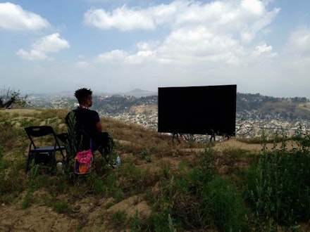 Erin Christovale facing black screen on hilltop of Elysian Park, with view of North East L.A. and the Los Angeles River. Photo: Rafa Esparza.