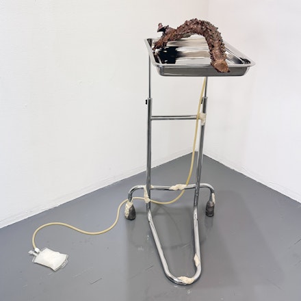 Nicki Cherry, <em>After the flame, after the pain</em>, 2022, bronze, stainless steel surgical instrument stand, beeswax, cotton gauze, epoxy clay, rubber tubing, IV bag, oil of milk, 43 x 32 x 48 inches. Courtesy GHOSTMACHINE. 